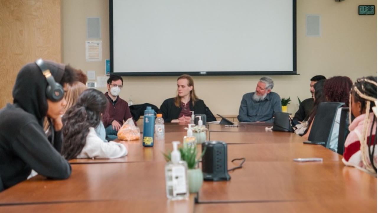 A group of students sitting around a table and listening to a Panel